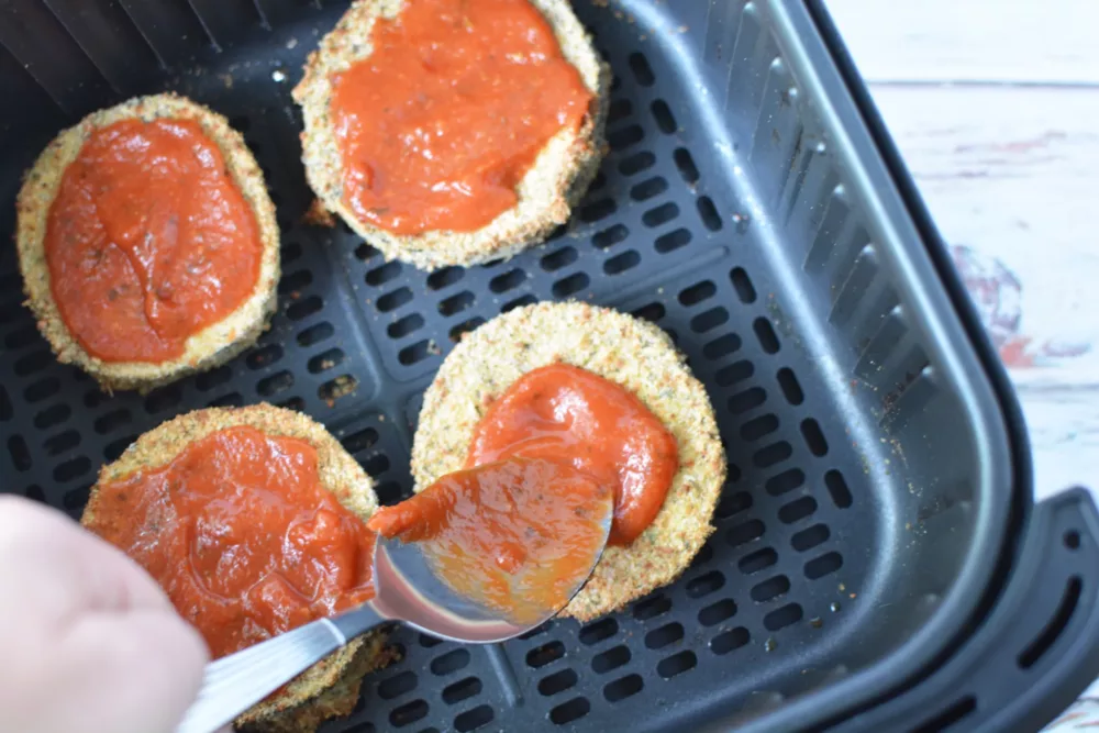 marinara sauce being spooned onto breaded slices of eggplant