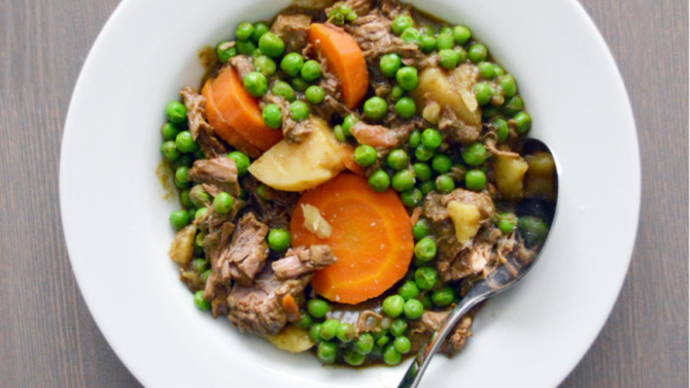 A bowl of vegetable beef stew with carrots and peas.
