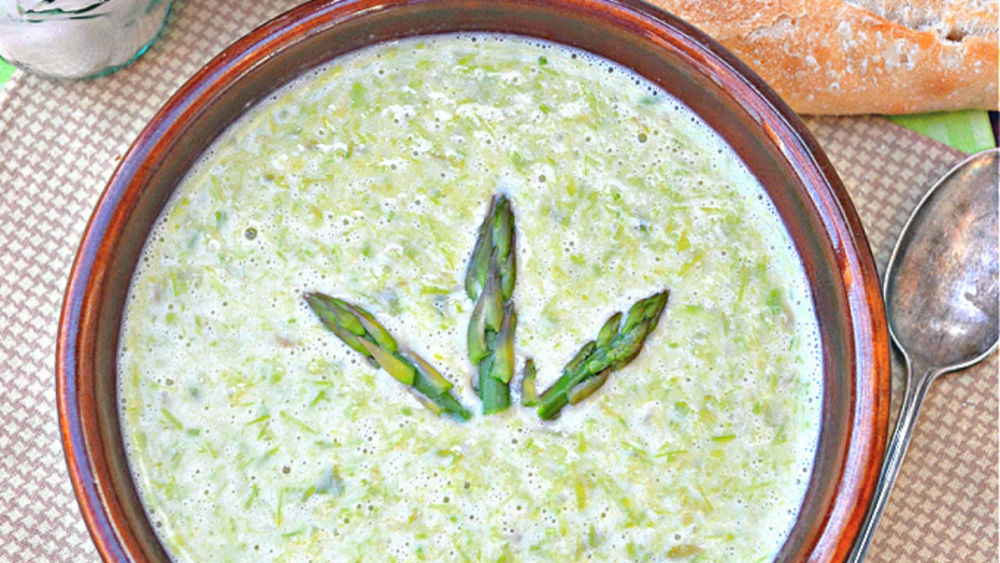 A bowl of cream of asparagus soup with three asparagus tips on top.
