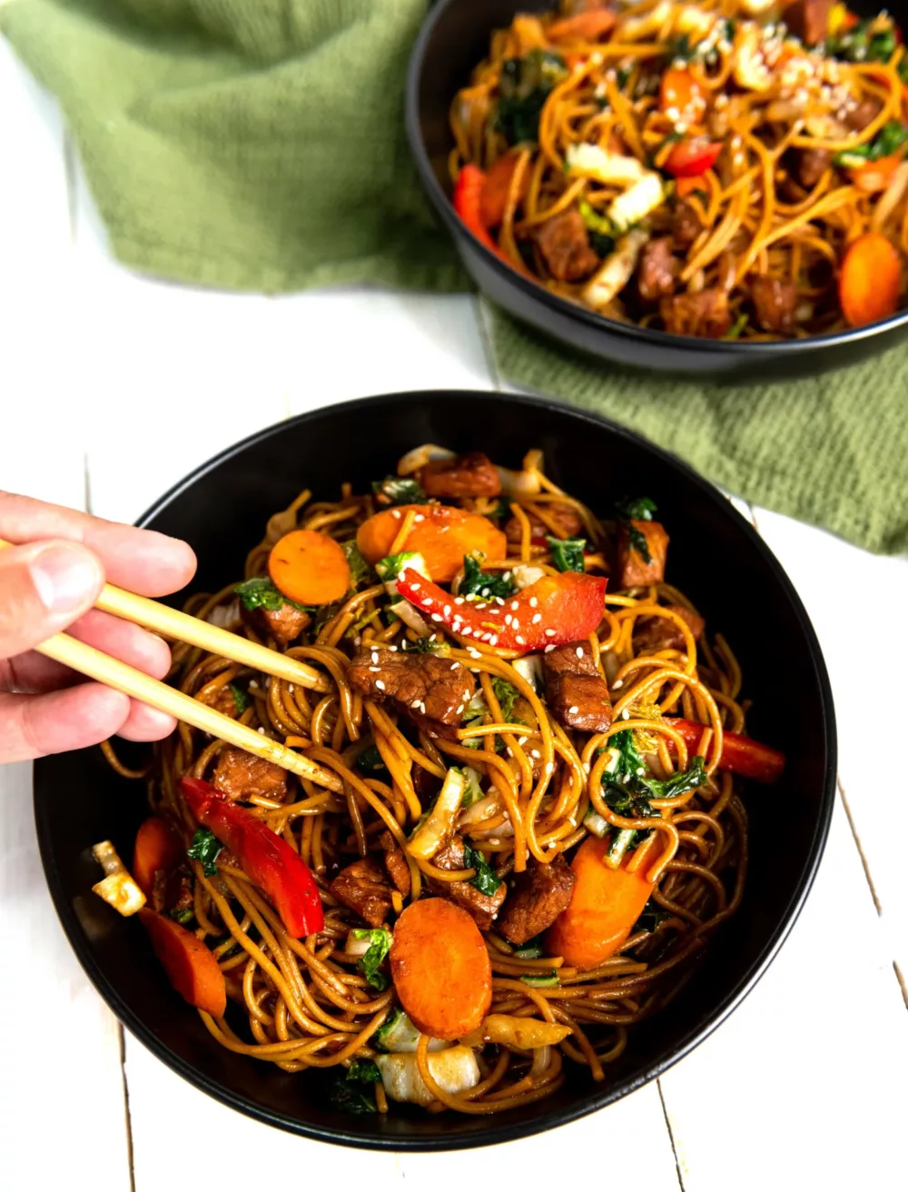 veggies and noodles in a black bowl with chopsticks