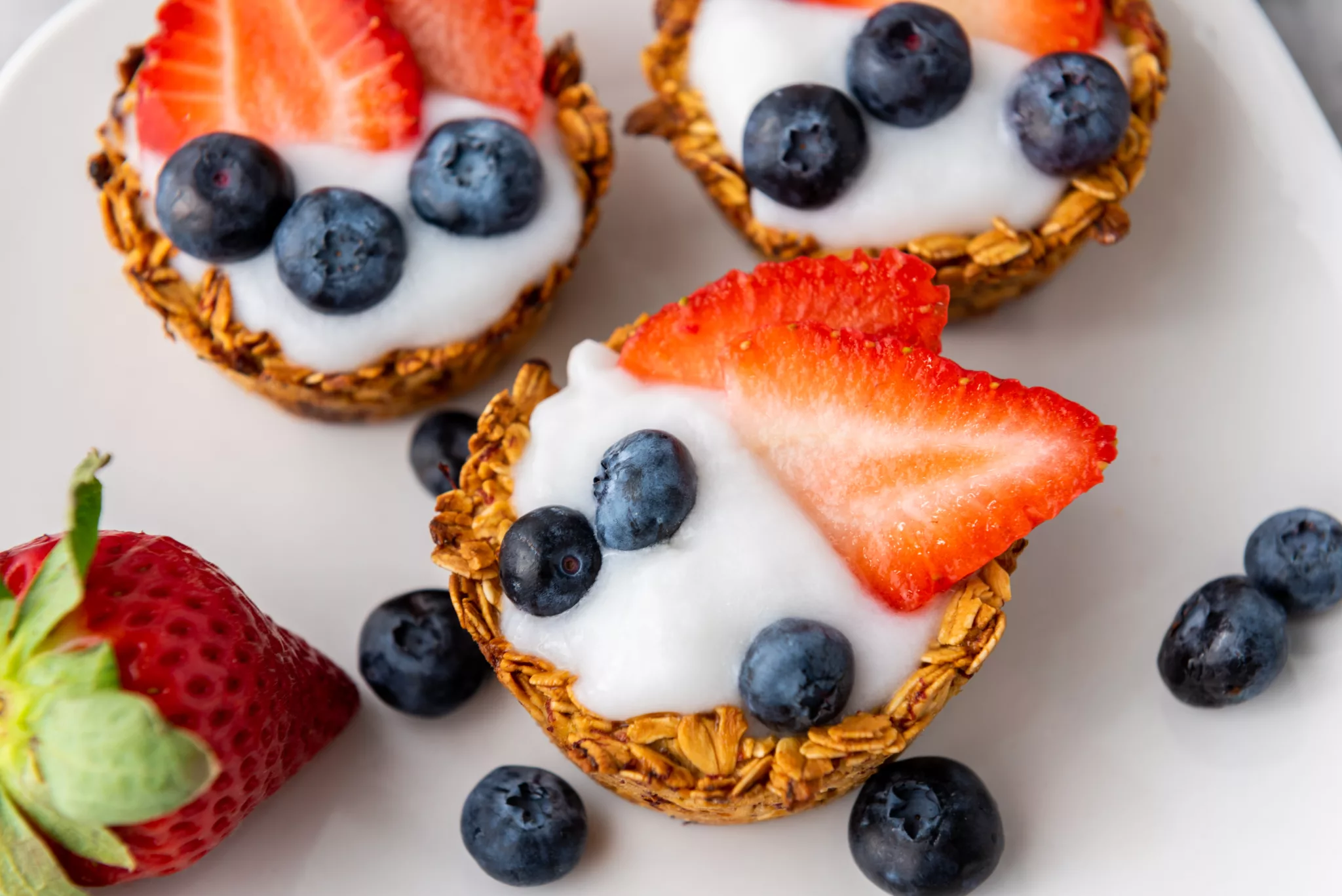 Granola Cups filled with yogurt and fresh blueberries and strawberries on a white plate