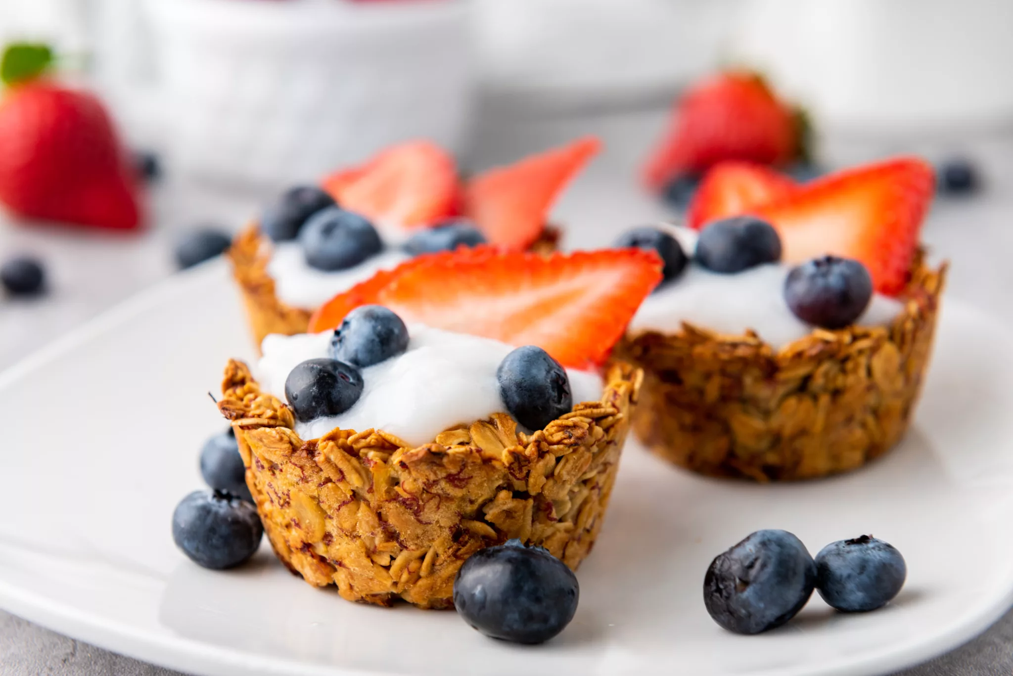Granola Cups filled with yogurt and fresh blueberries and strawberries on a white plate