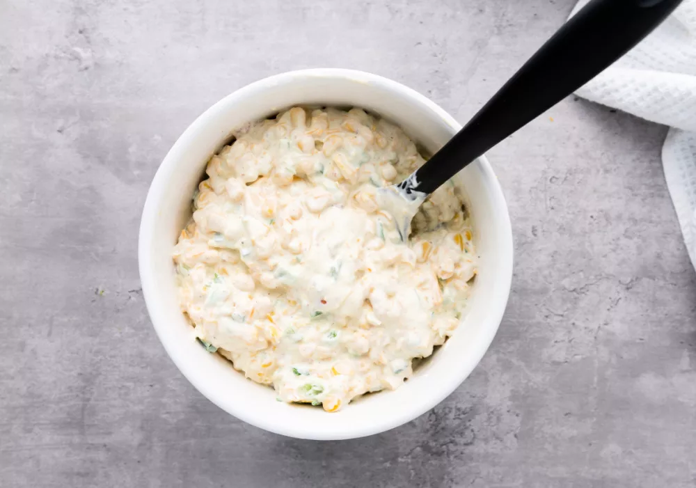bowl of shredded cheddar cheese, corn, mayonnaise, sour cream, scallions, bacon and jalapenos