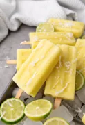 yellow popsicles with shaved coconut on top and limes in the background