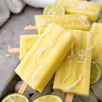 yellow popsicles with shaved coconut on top and limes in the background