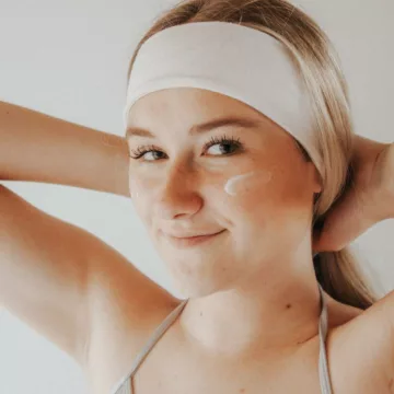 woman with her hair in a headband and moisturizer on her cheek