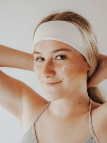 woman with her hair in a headband and moisturizer on her cheek