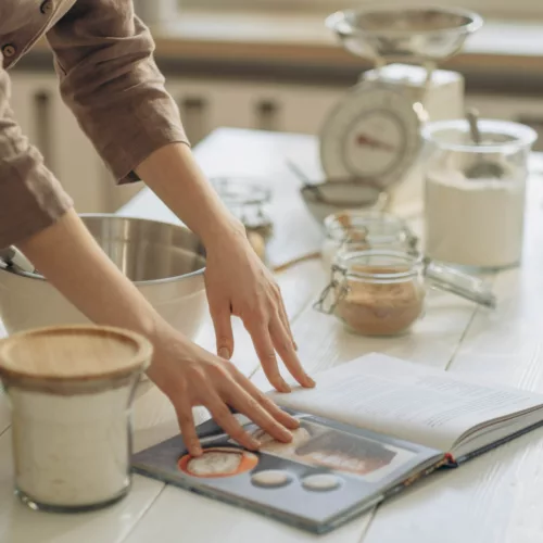 person thumbing through a cookbook on their kitchen counter