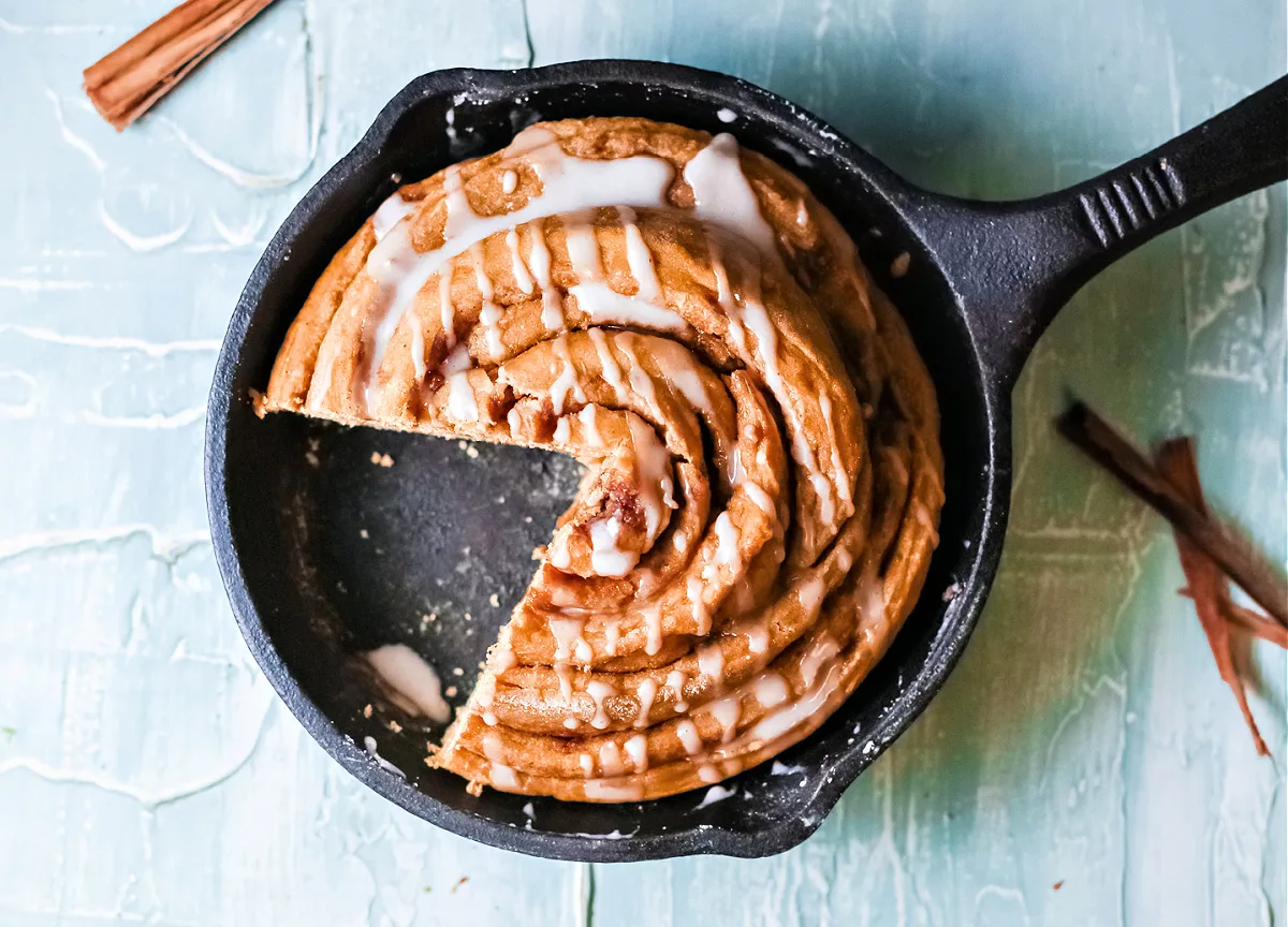cast iron skillet with a cinnamon roll cake shaped like a pie covered in white frosting