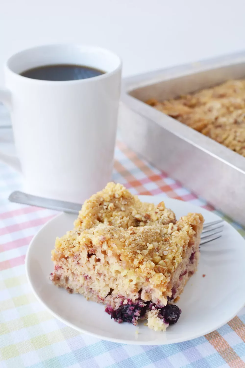 Closeup shot of piece of berry cake on plate with a mug of coffee next to it. 