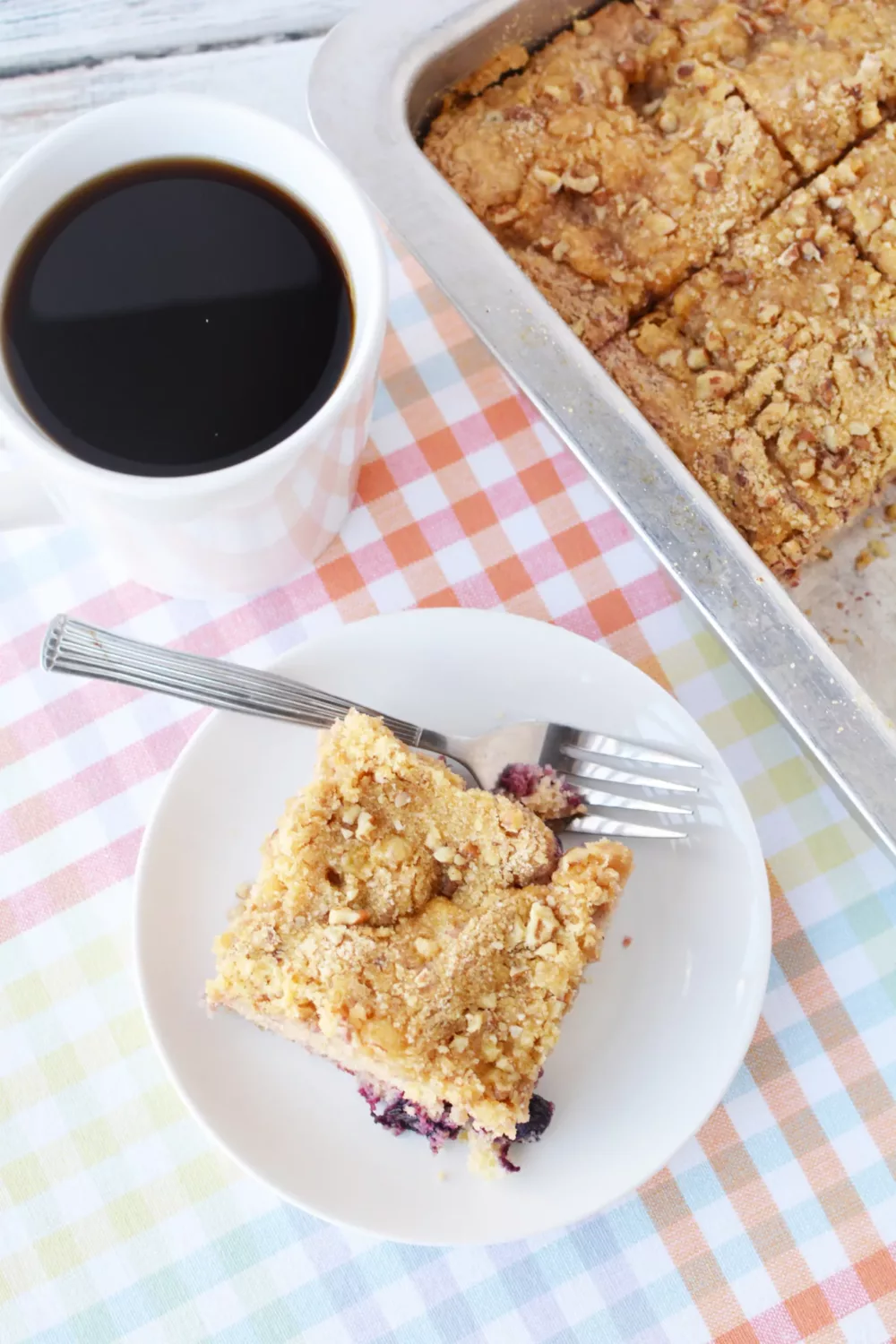 Overhead shot of slice of berry cake next to mug of coffee and baking dish with more cake.
