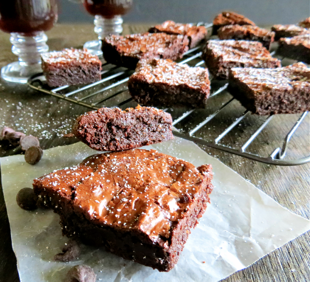 Dairy free brownies on parchment paper with more brownies on cooling rack in background. 