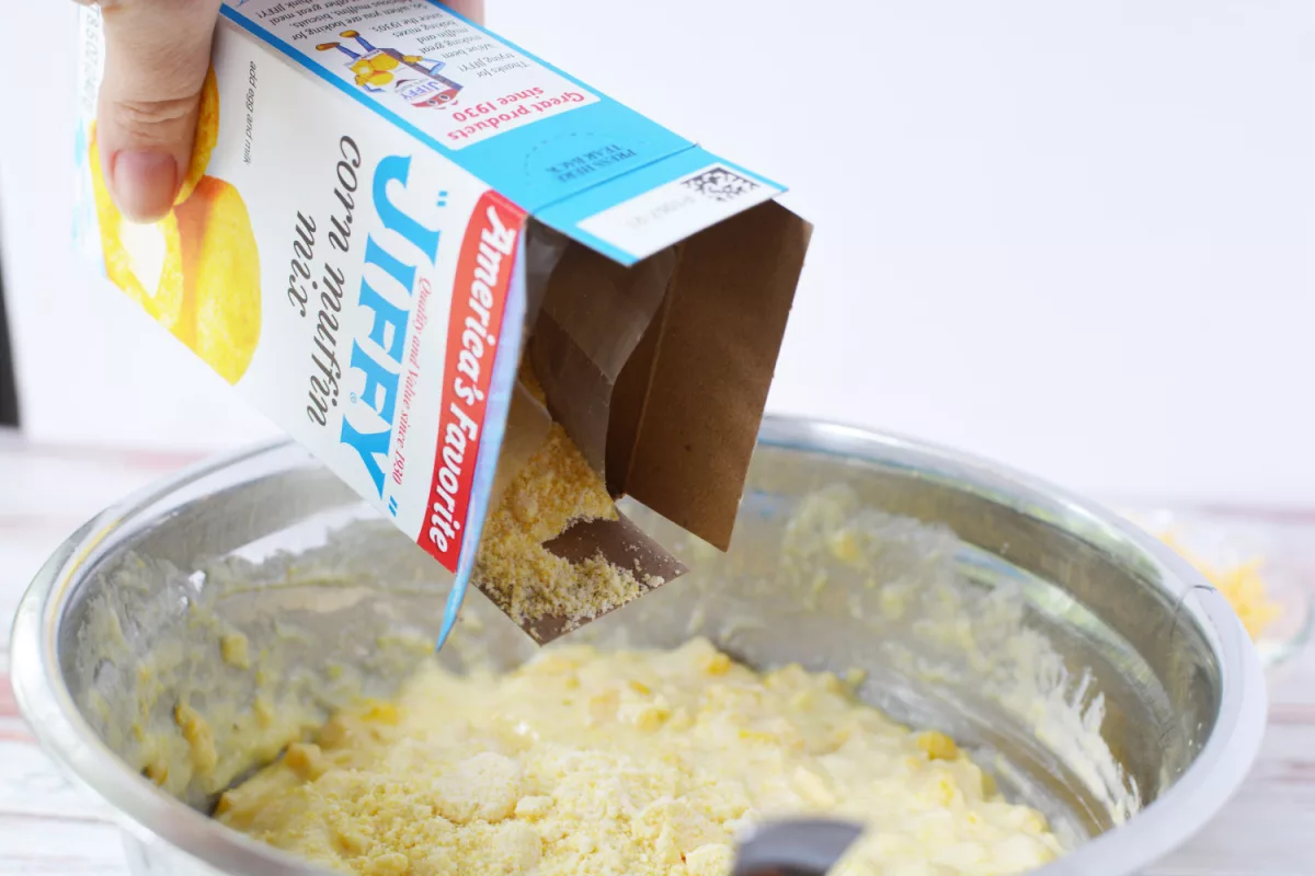 box of Jiffy cornbread mix being poured into a large mixing bowl