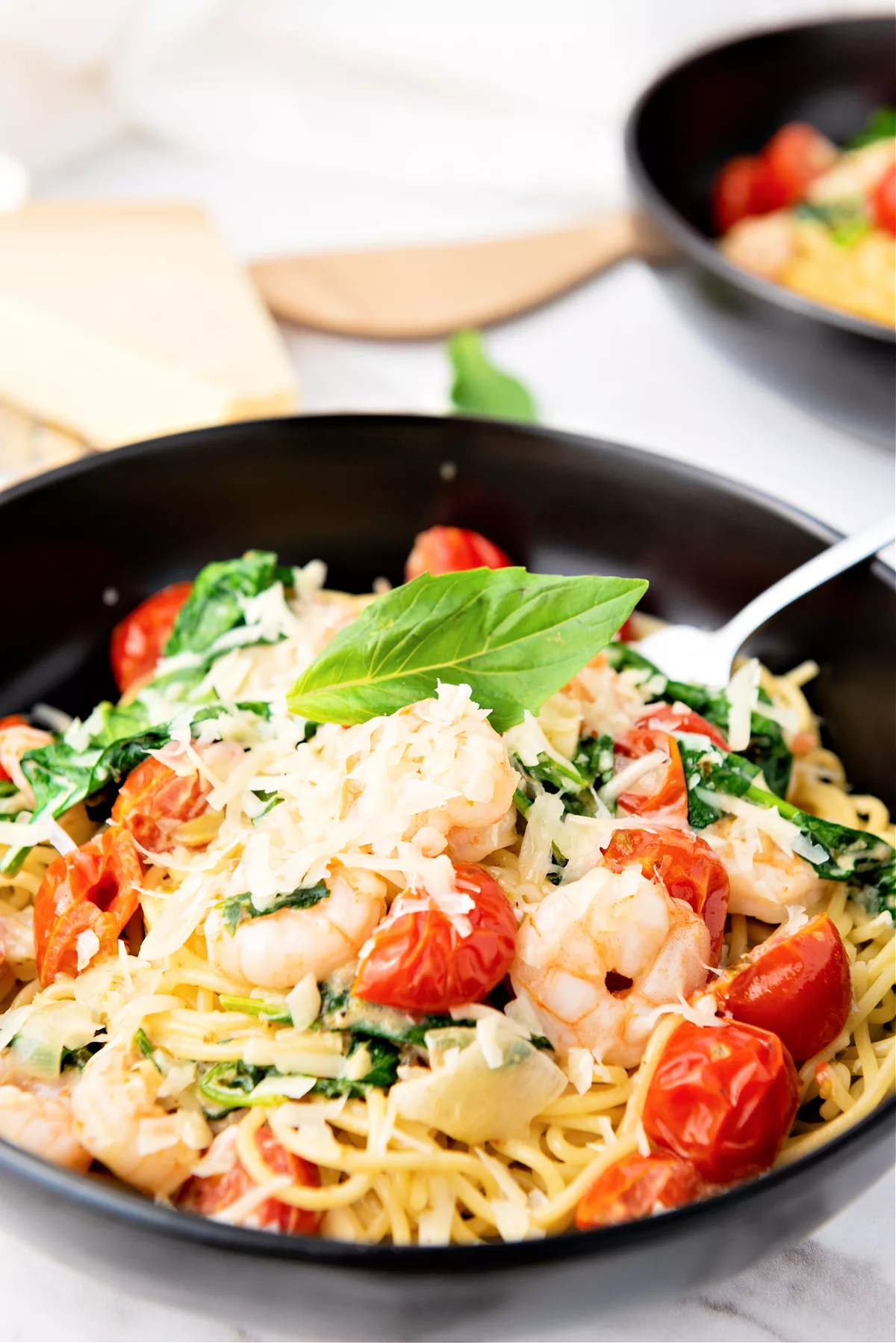 Overhead shot of fork in a bowlful of shrimp scampi with angel hair pasta, filled with cherry tomatoes and spinach and grated cheese