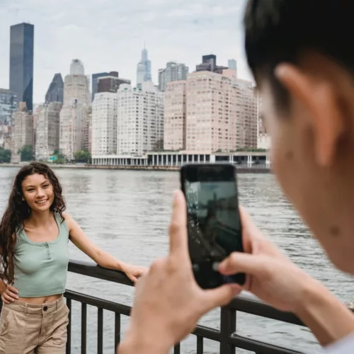 person taking photo of a woman with long hair against the NYC skyline with a phone