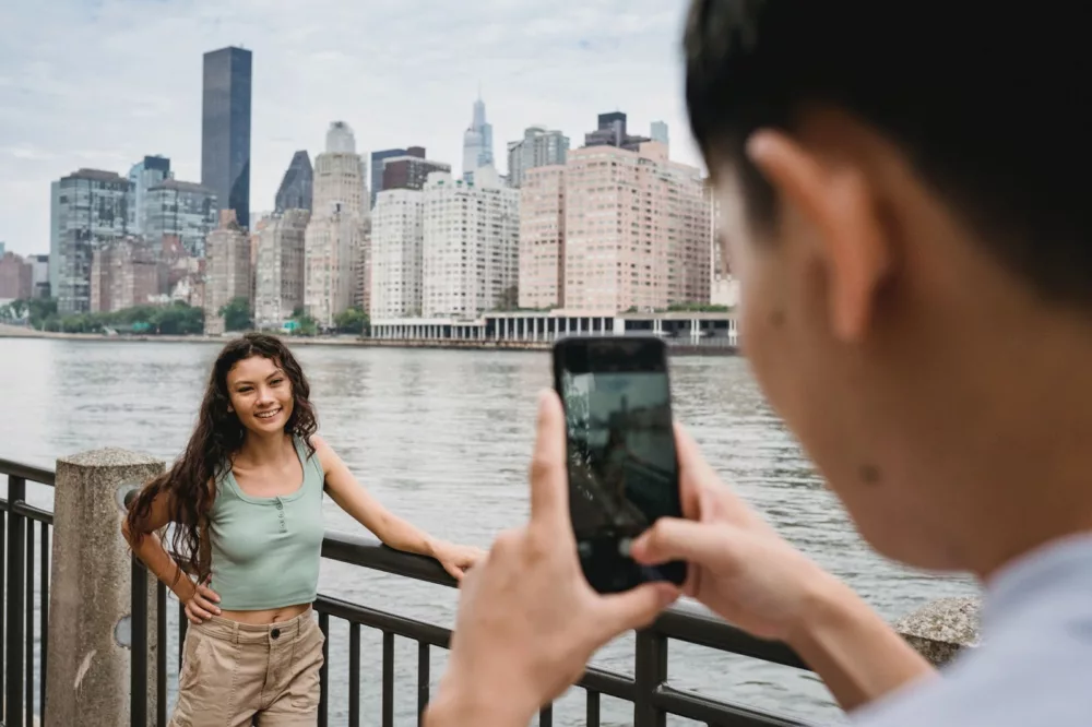 person taking photo of a woman with long hair against the NYC skyline with a phone