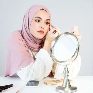 woman in a head scarf doing her eye makeup
