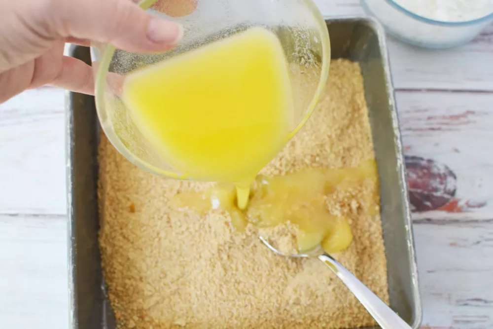 Overhead shot of butter being poured into baking dish with graham cracker crumbs. 