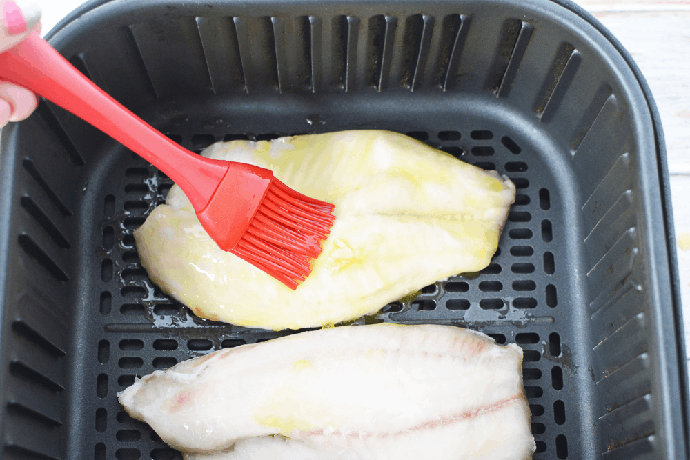 Frozen fish fillets in air fryer being brushed with olive oil
