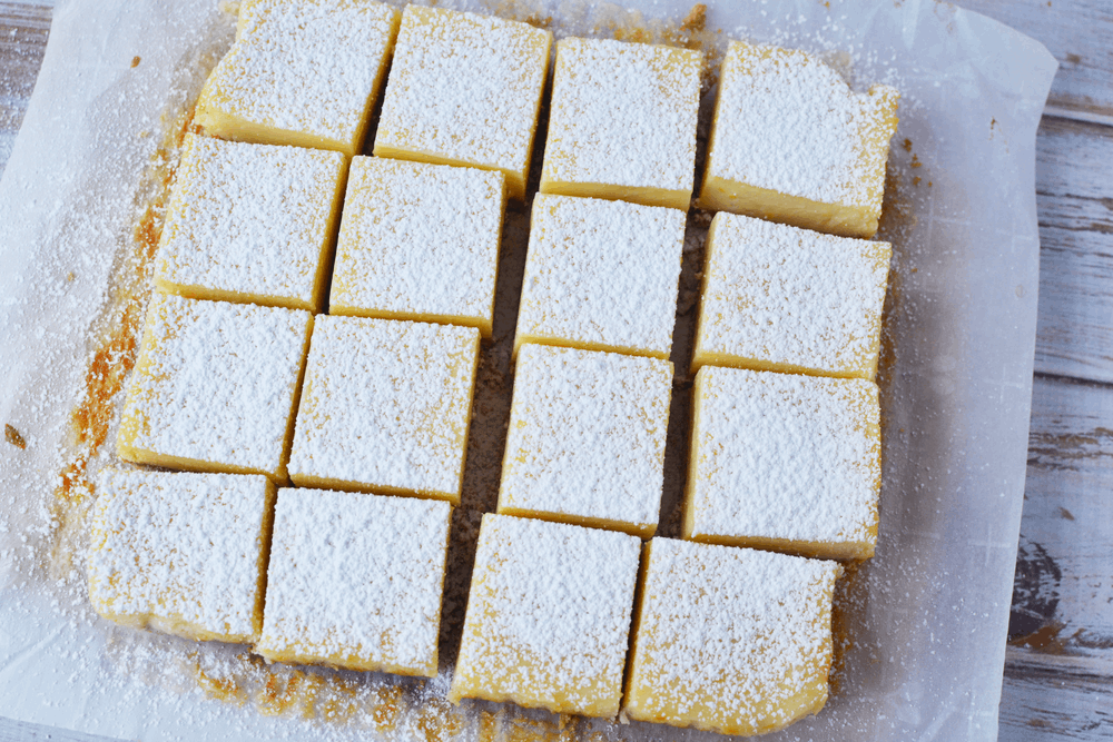 Overhead shot of lemon bars with graham cracker crust topped with powdered sugar on parchment paper. 