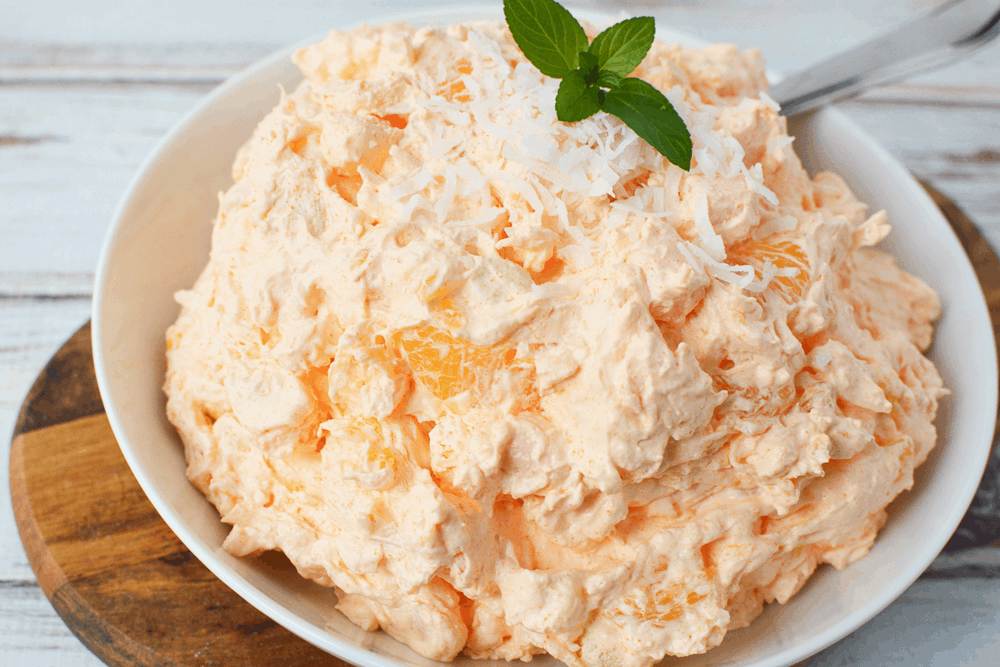 Orange JELLO Salad filled with mini marshmallows, pineapple, shredded coconut in a bowl