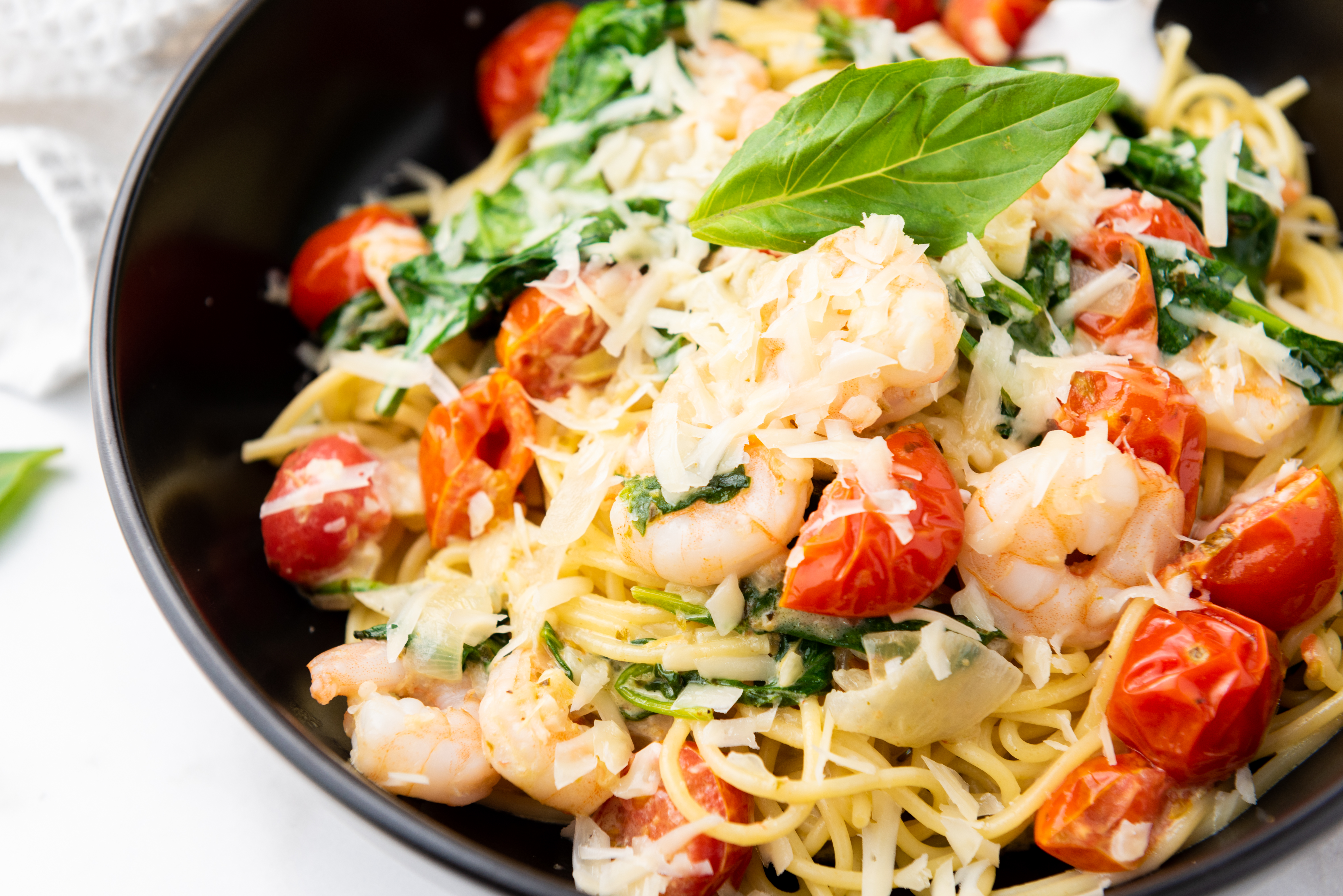 Overhead shot of fork in a bowlful of shrimp scampi with angel hair pasta, filled with cherry tomatoes and spinach and grated cheese
