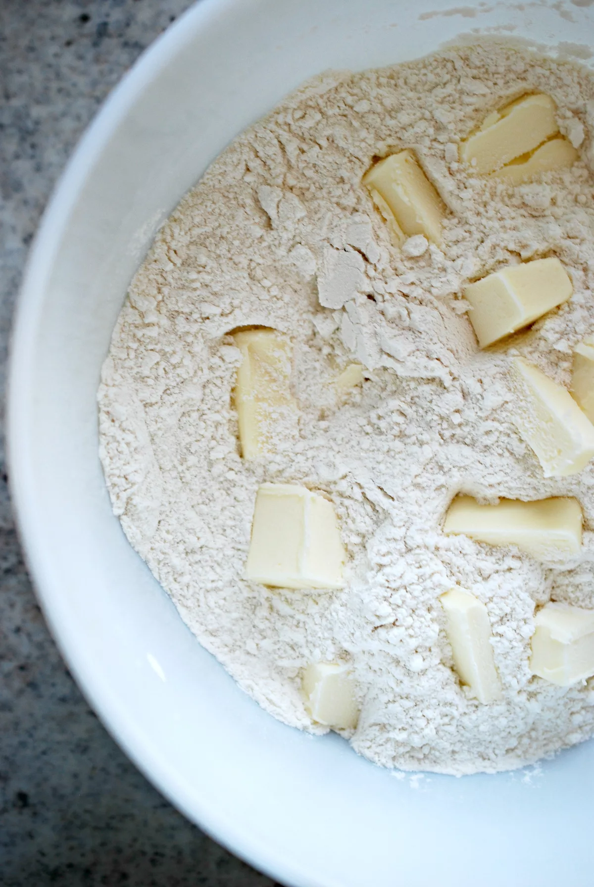 Overhead shot of bowlful of sugar, flour, and baking powder with chunks of butter.