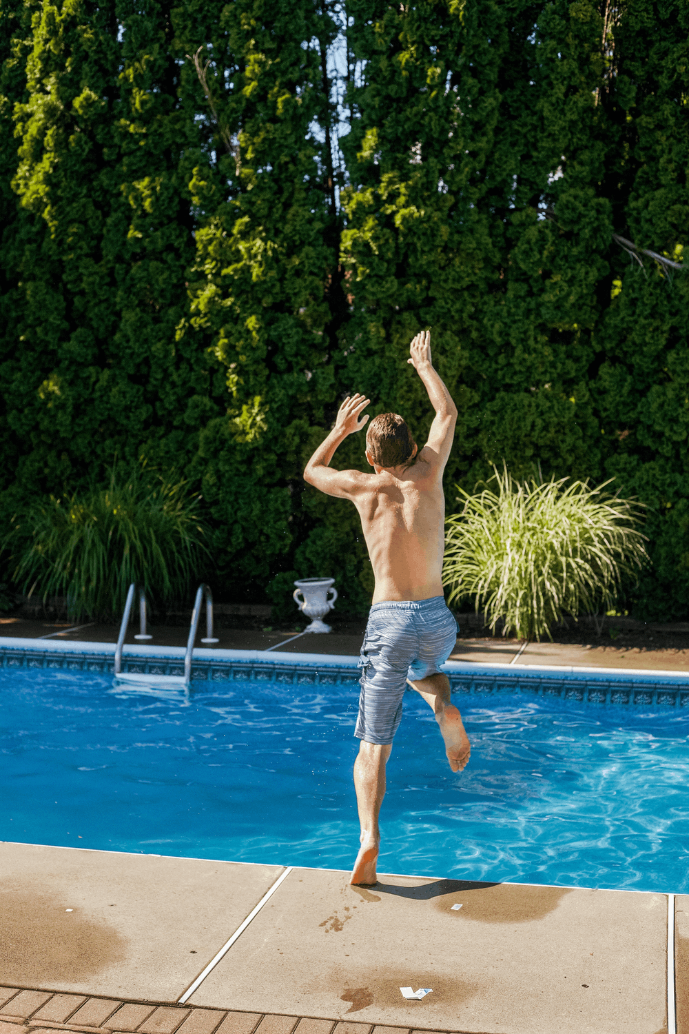 kid jumping into a pool in swim trunks