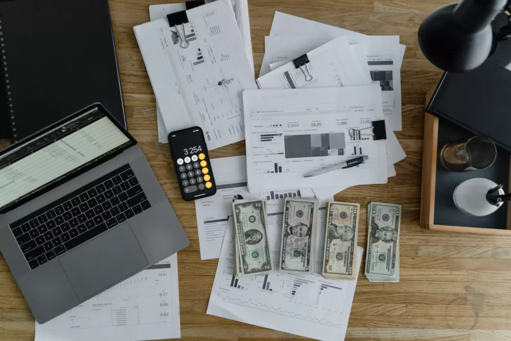 laptop paperwork and money on a desk
