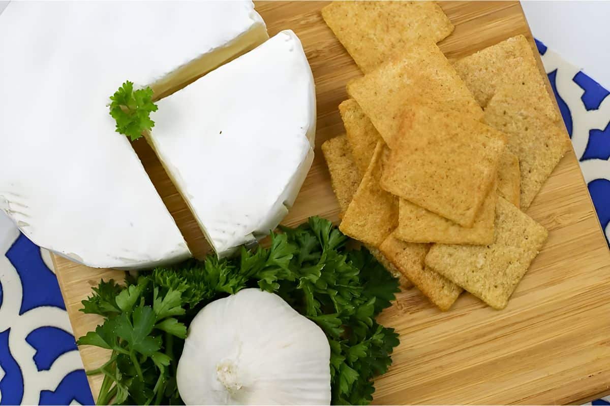 wheel of brie cheese a bulb of garlic and a spread of crackers and parsley
