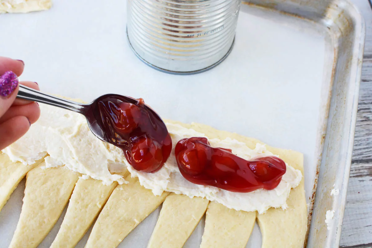 cherry pie filling being put on a cream cheese mixture on crescent rolls