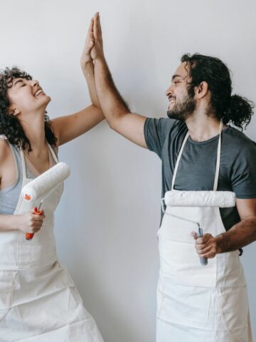 a couple in aprons holding paint brushes giving each other the high five