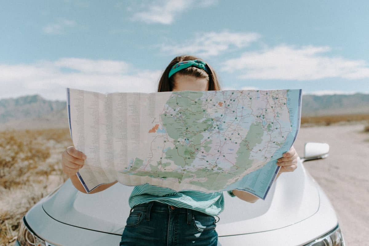 woman holding a road map in front of her car on a road trip