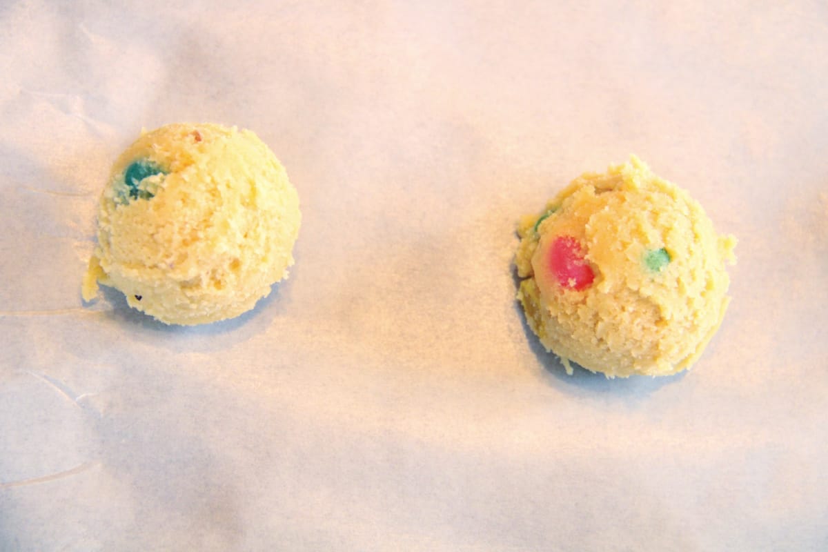 Overhead, closeup shot of two scoops of jelly bean cookie dough on baking sheet.