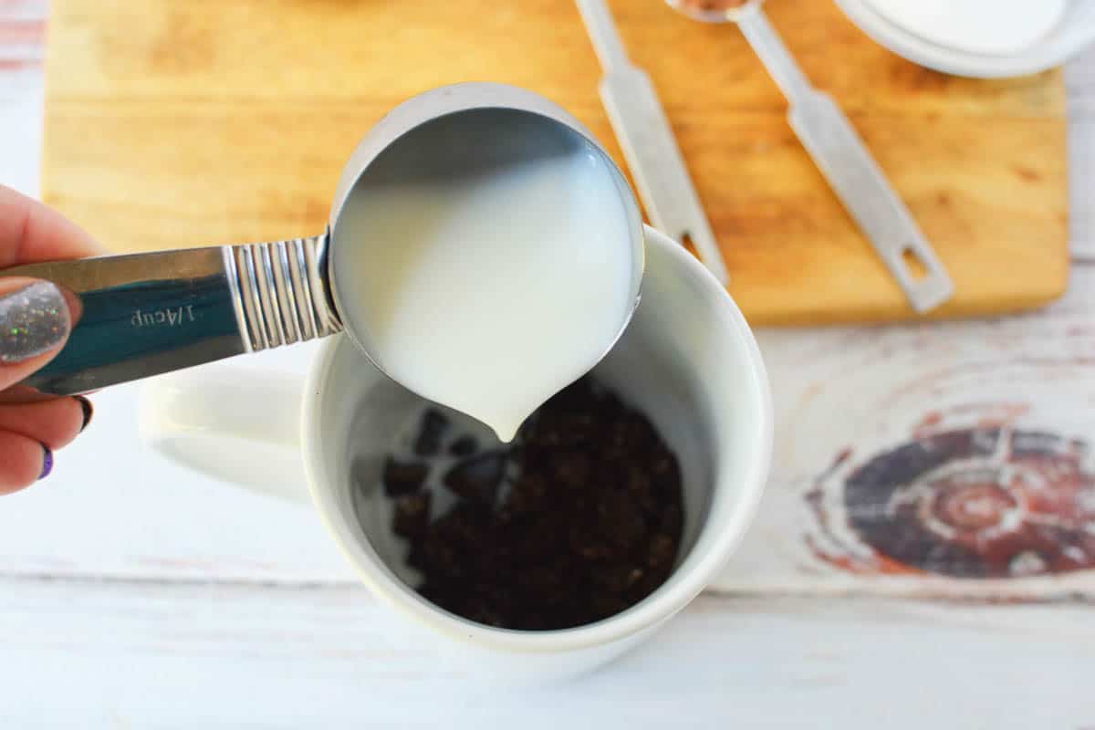 Milk being poured into mug with sugar and crushed Oreos. 