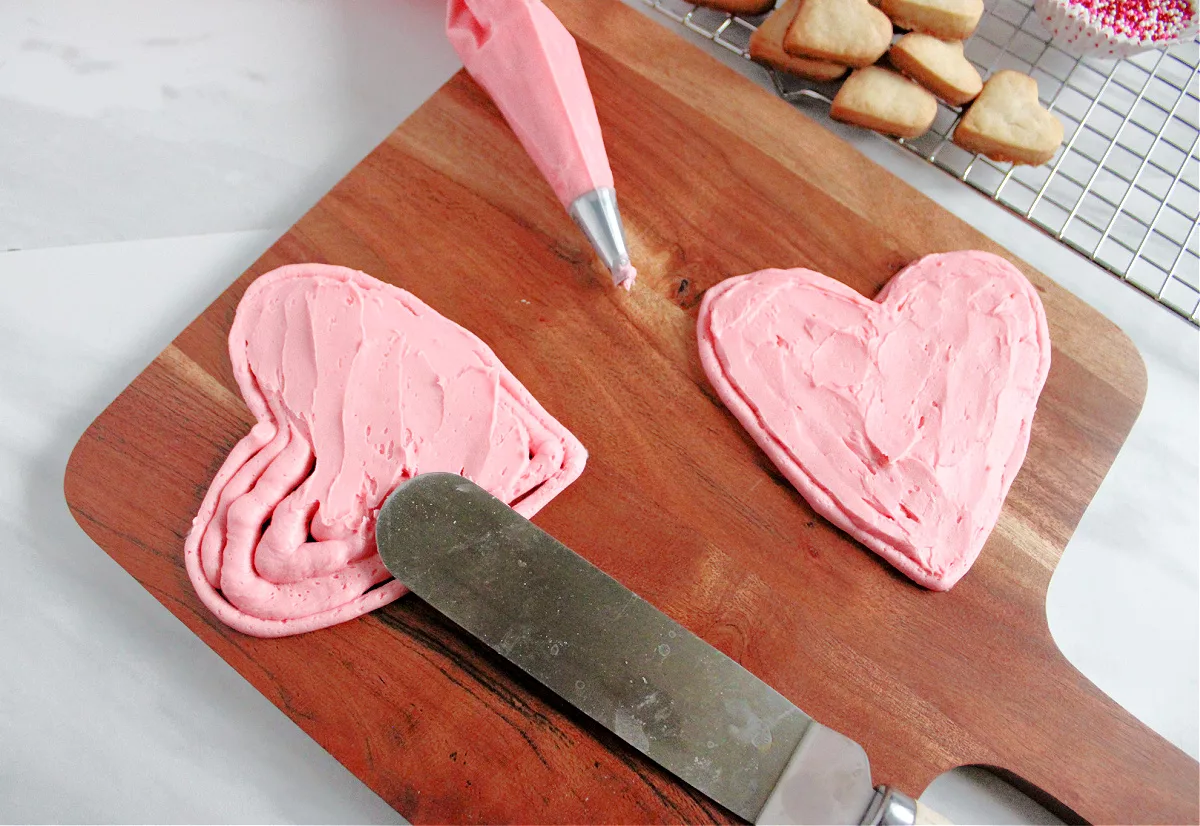 pink buttercream frosting being piped onto a wooden board in the shape of a heart