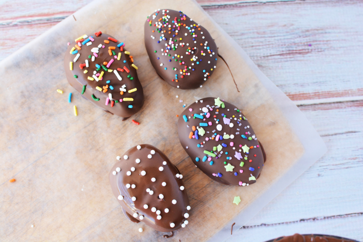 Four chocoalte easter eggs coated in chocolate almond bark and sprinkles on cutting board