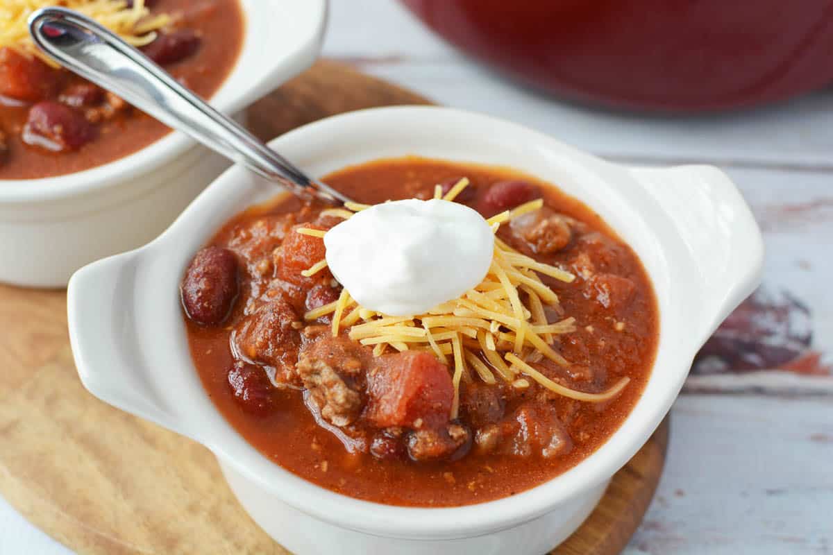 Dutch Oven Chili in white bowls topped with shredded cheddar cheese and a dallop of sour cream
