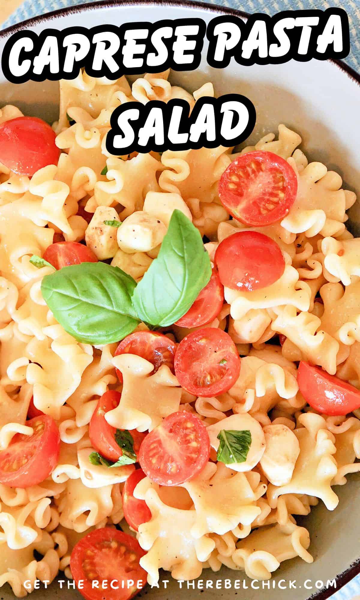 Overhead view of a bowl of pasta salad filled with cherry tomatoes and mozzarella pearls and fresh basil