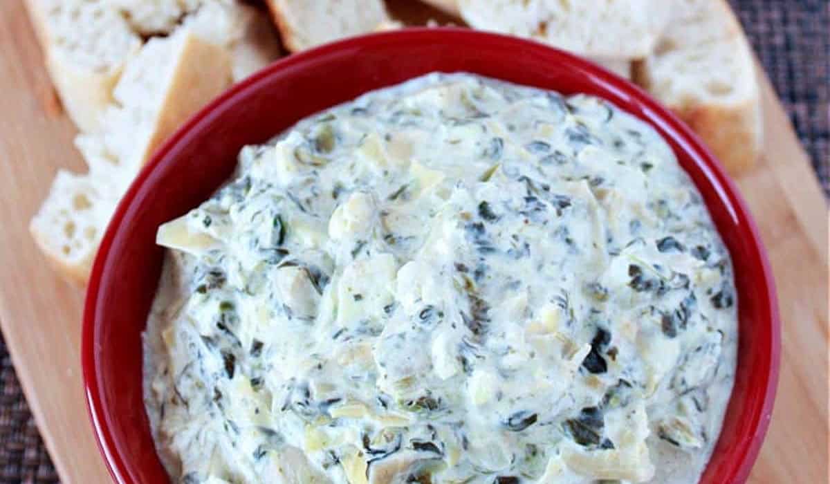 Spinach and Artichoke Dip in a red bowl with crusty bread around it