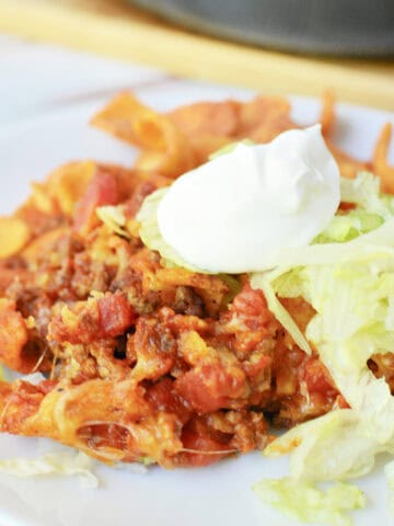 Walking Taco Casserole on a white plate topped with shredded lettuce and sour cream