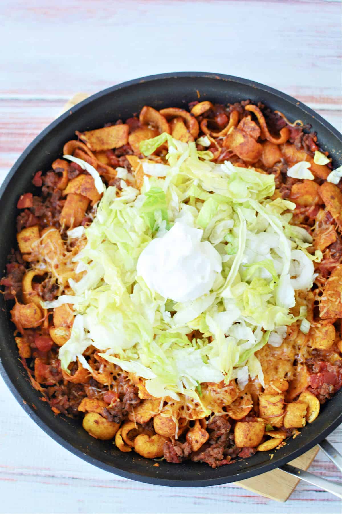 Walking Taco Casserole in a cast iron pan topped with shredded lettuce and sour cream