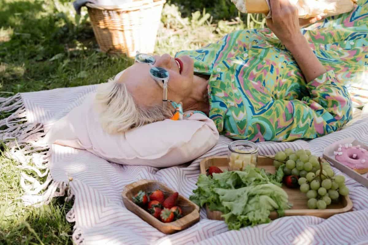 senior woman laying on a blanket having a picnic with wine