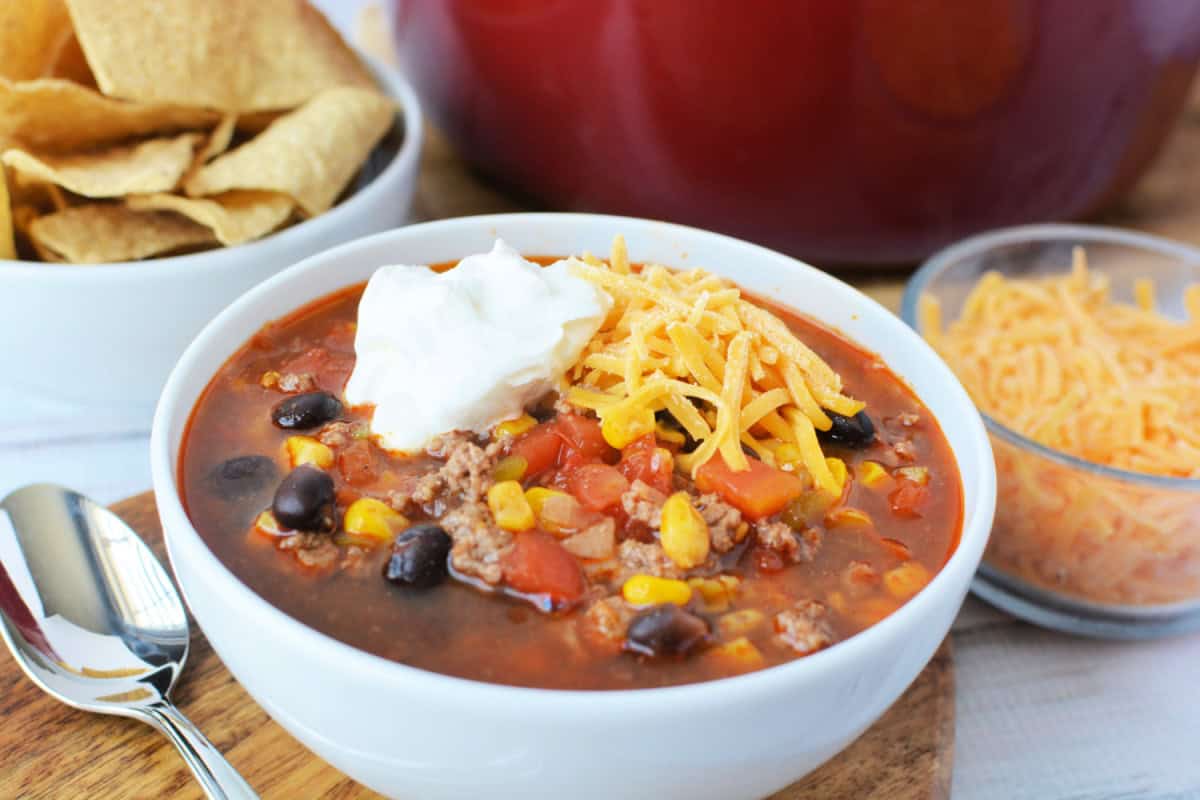 Beef Enchilada Soup topped with shredded cheddar cheese and a scoop of sour cream