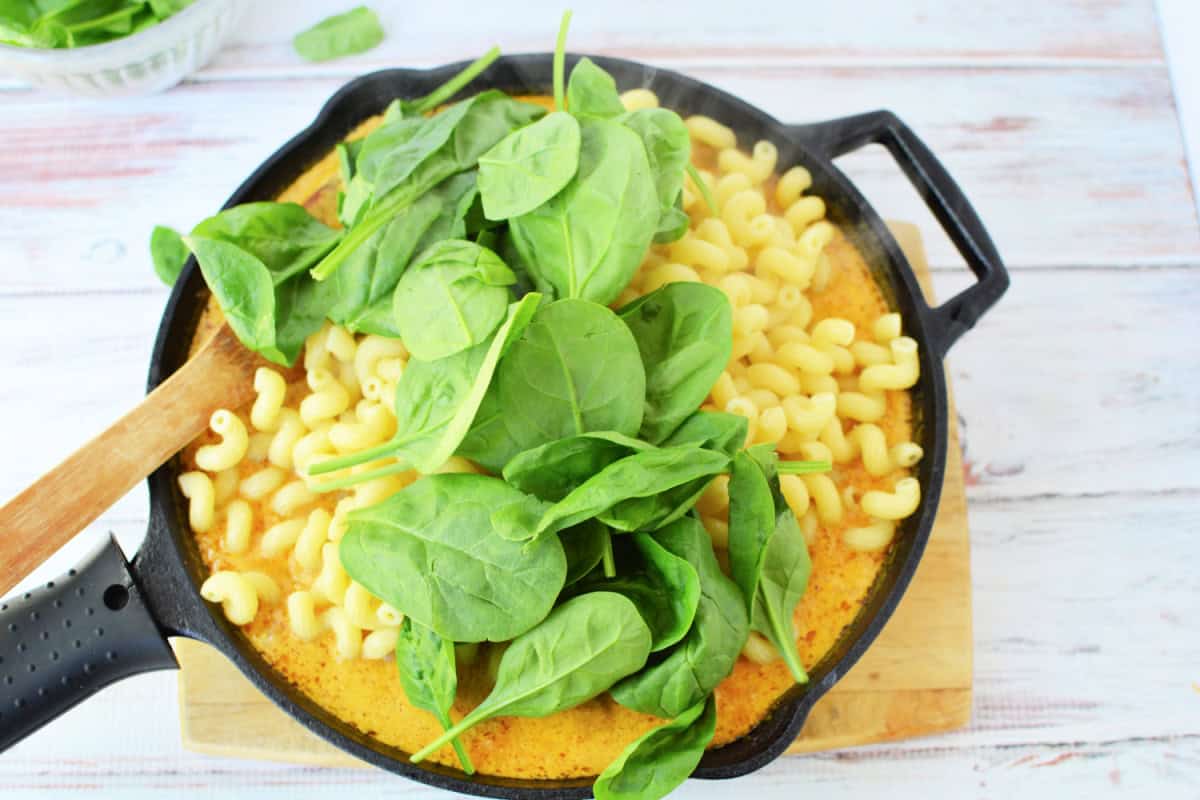 fresh spinach on top of pasta in a skillet