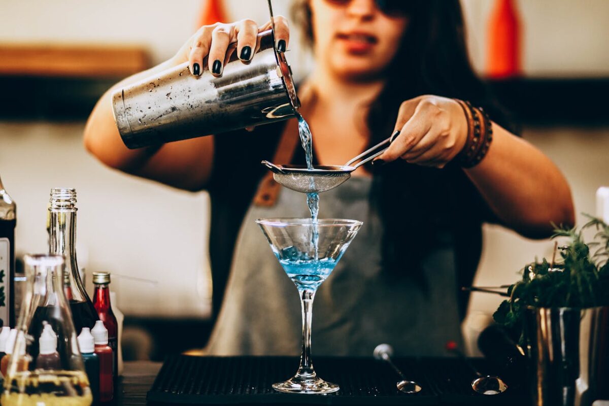 woman making cocktails in a martini glass with blue liquor