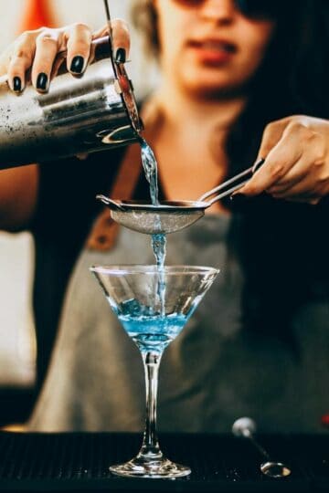 woman making cocktails in a martini glass with blue liquor
