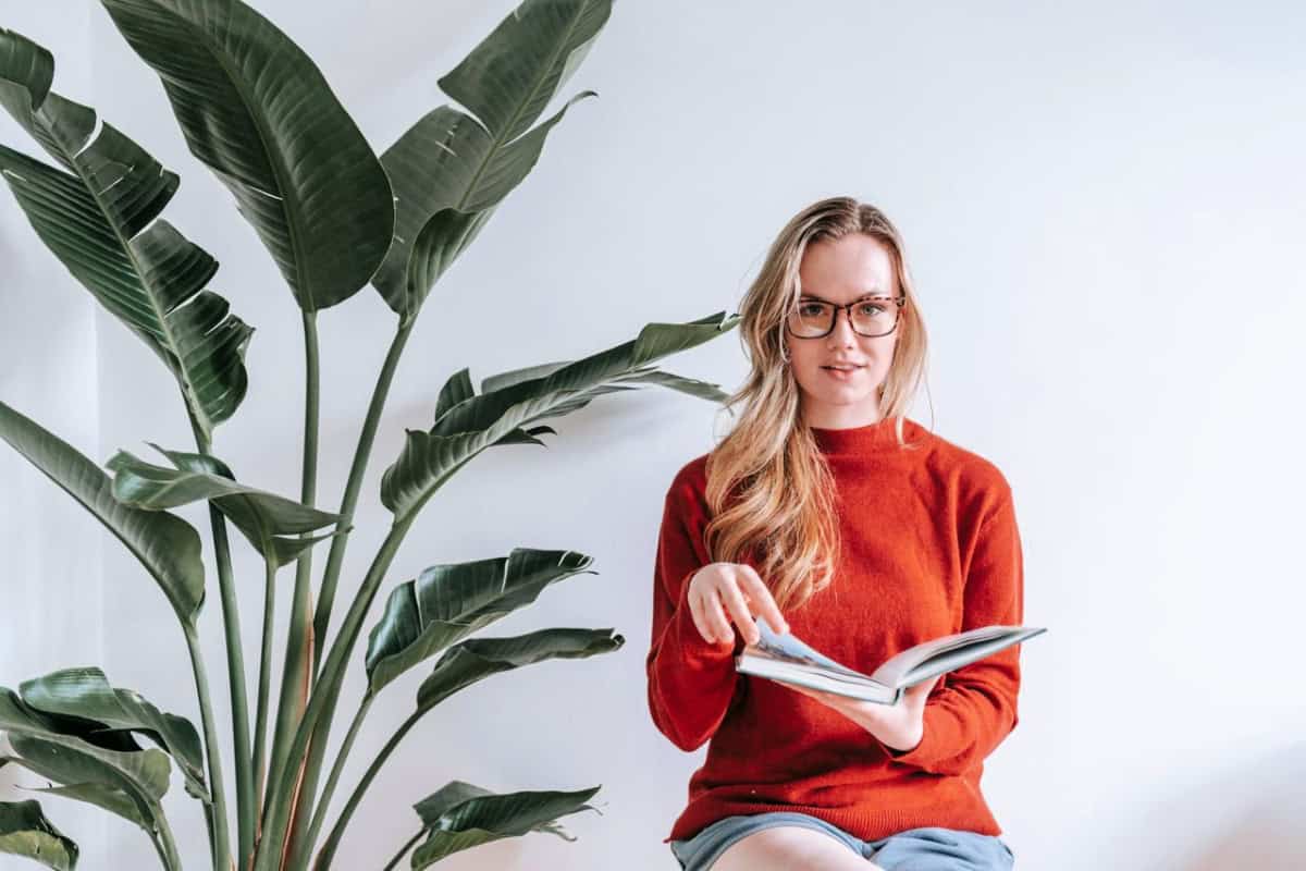woman in a red sweater reading a book near a houseplant
