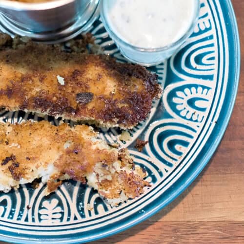 Crispy homemade chicken strips served with dipping sauces on a decorative plate.