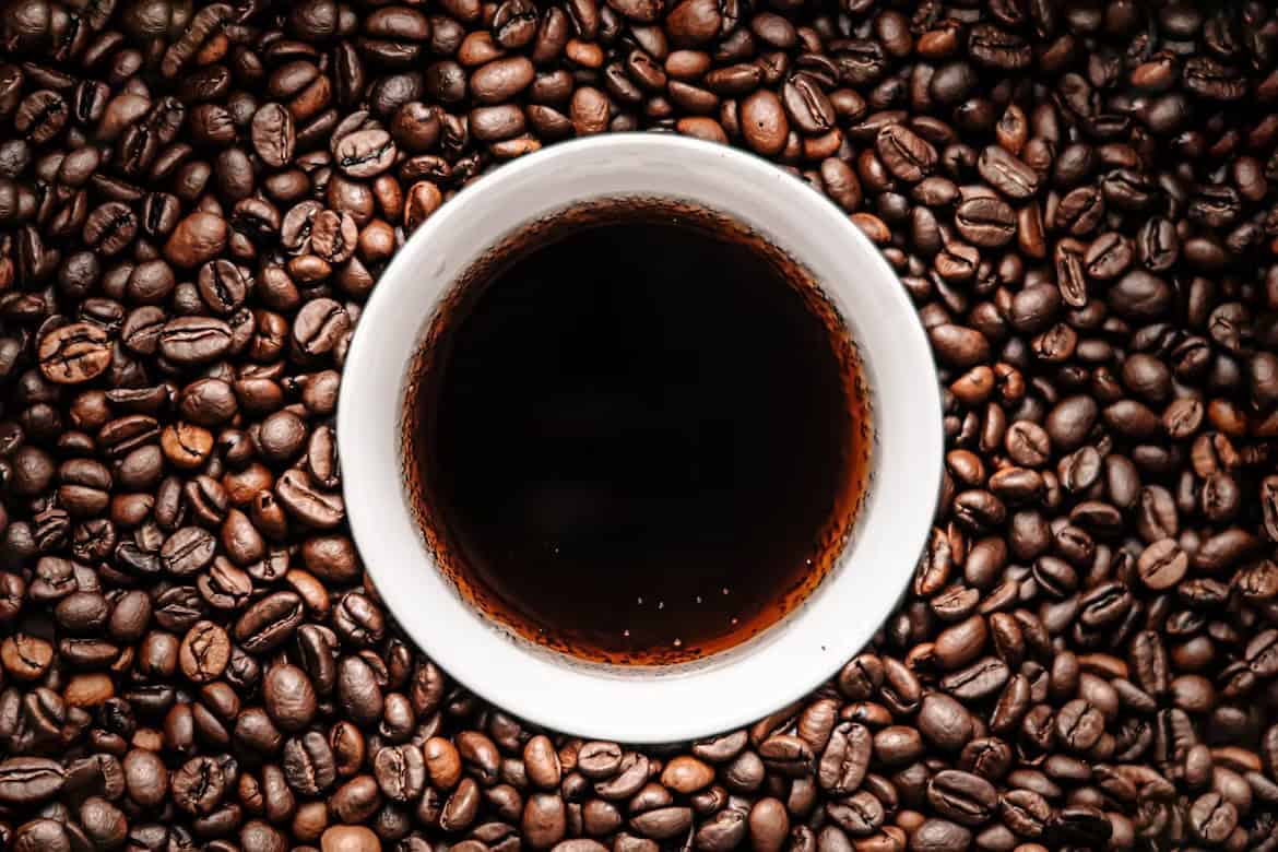 a cup of low acid coffee surrounded with coffee beans